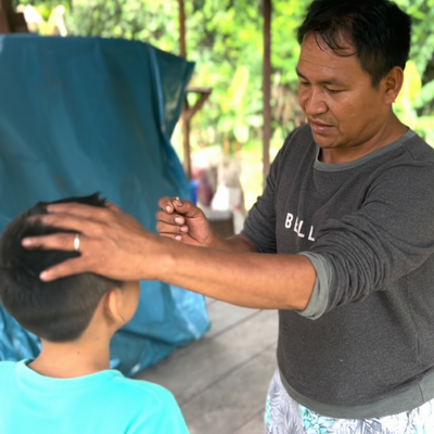 Man shipibo and child interacting outdoors with a blue tarp in the background