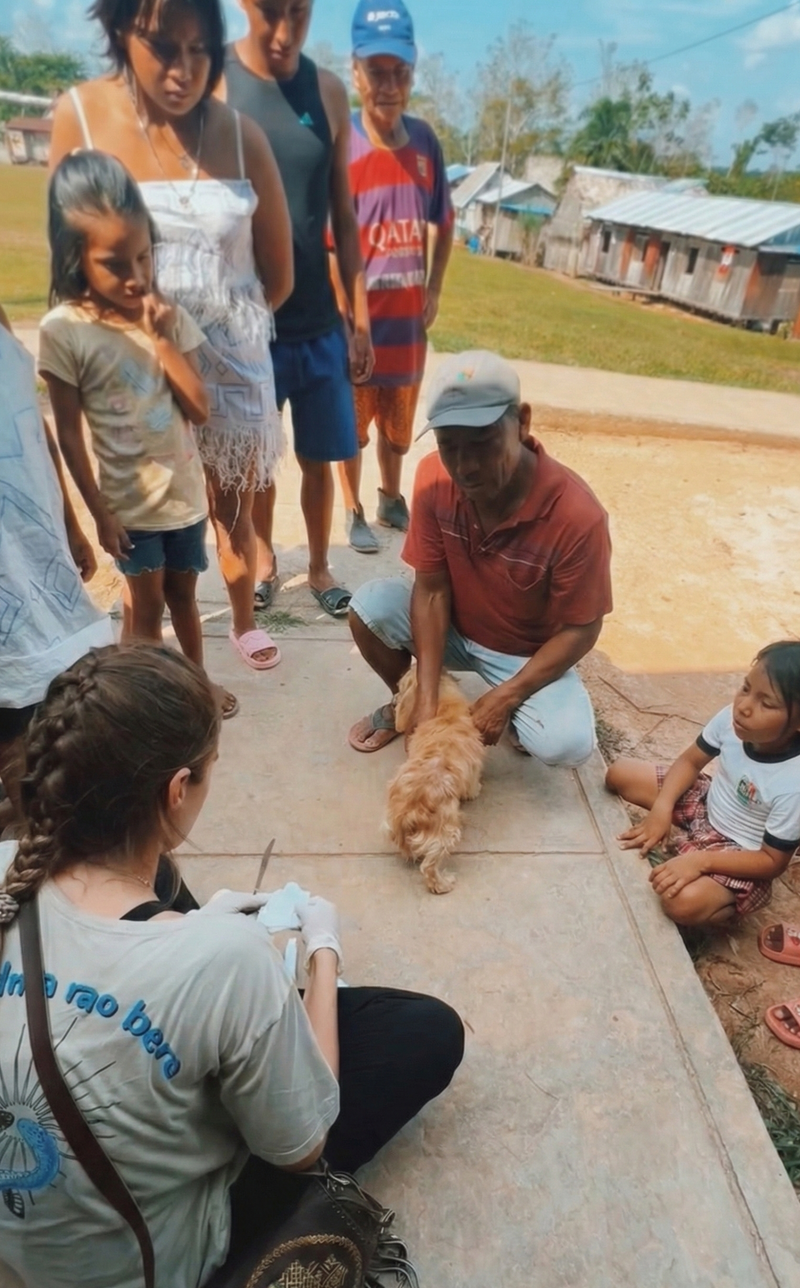 Group of people, including children, gathered around a small dog on a concrete surface.