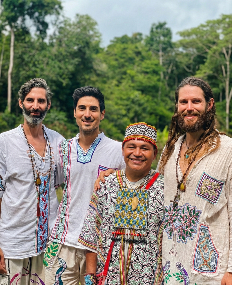 Four men, three in modern clothing and one in traditional attire, standing in a forest.